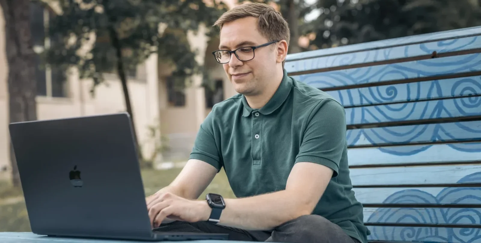 Nicolas Wazulek (wearing a green shirt) working outside on a big blue bench to enjoy the weather and finding creative solutions for the software being developed.